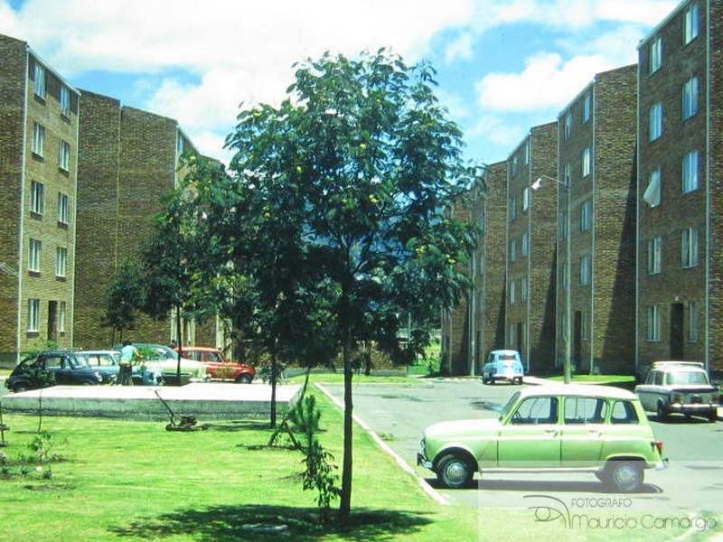 Fotografía de la unidad residencial El Guali construida por la Caja de Vivienda Popular en la localidad de Engativá, en la que se retrata la vista interior de la zona verde, los bloques habitacionales y los parqueaderos (1970). 